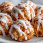 Close-up of several warm, gooey cinnamon roll bites drizzled generously with thick white icing.