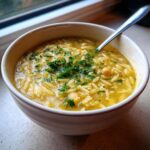 A close-up of a warm bowl of chickpea soup featuring orzo pasta and topped with fresh parsley.