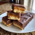A stack of homemade twix bars showing the shortbread base, gooey caramel layer, and chocolate coating.