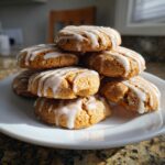 A stack of soft, spiced persimmon cookies drizzled with white icing, presented on a white plate.