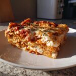 A thick, layered slice of instant pot lasagna topped with melted cheese and herbs, served on a white plate.