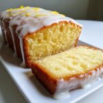 Close-up of a sliced lemon cake recipe loaf topped with white glaze and lemon zest.