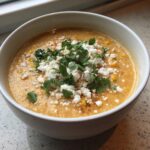 A close-up of a bowl of creamy mexican street corn soup topped generously with crumbled white cheese and fresh cilantro.