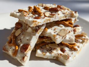 Close-up of stacked pieces of white chocolate peanut butter pretzel bark topped with almonds and pretzel pieces.
