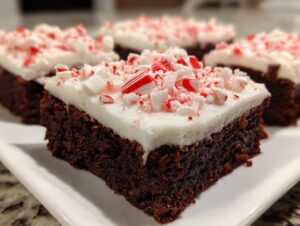 A close-up of a rich, fudgy peppermint brownie topped with thick white frosting and crushed candy canes.