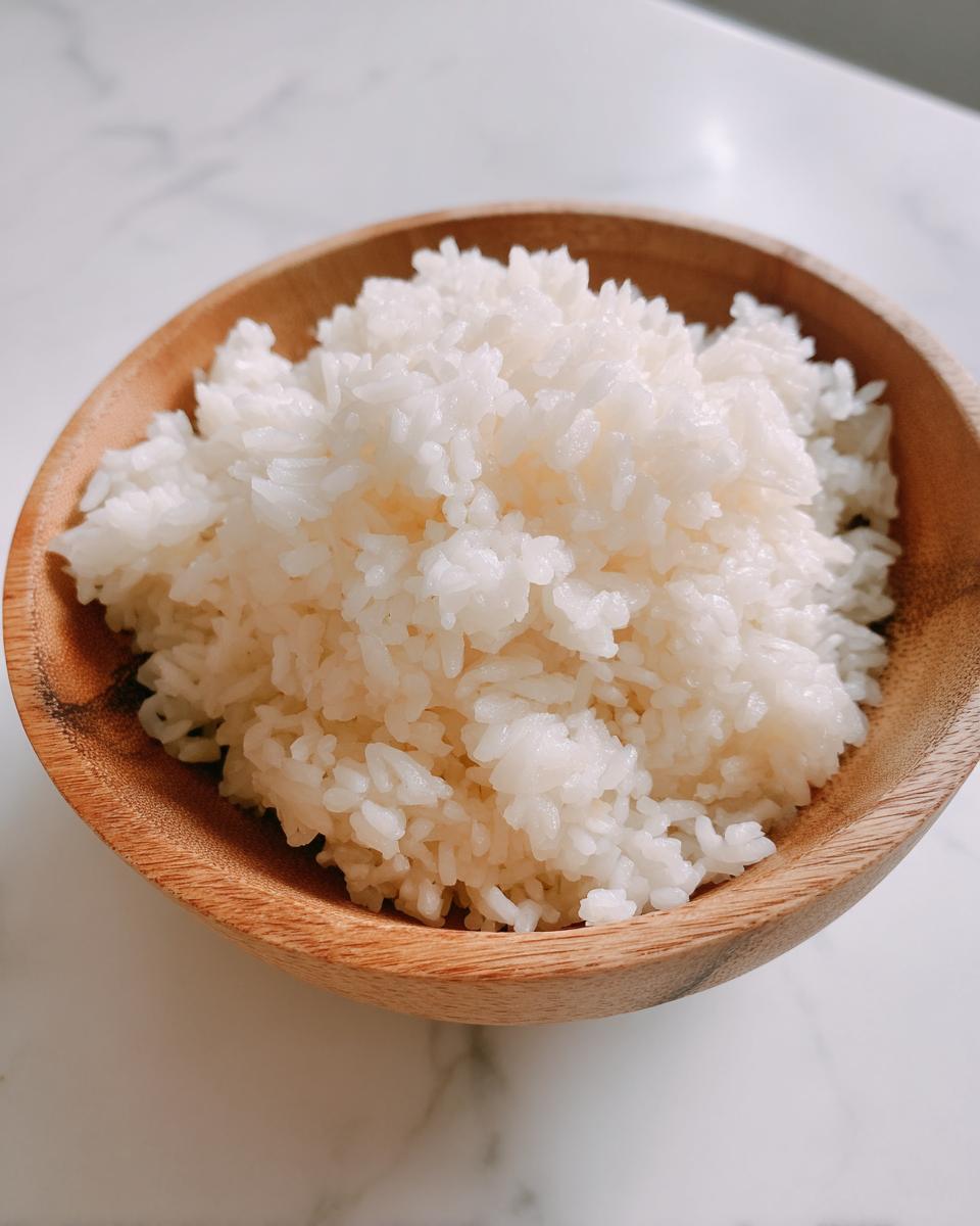 Close-up of perfectly cooked, glossy sushi rice mounded in a small wooden bowl.