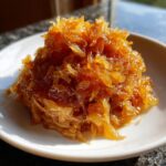 A close-up of a mound of deeply golden, glossy caramelized onions served on a small white dish.