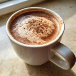 Close-up of a white mug filled with rich mexican hot chocolate, topped with foam and a dusting of spice.