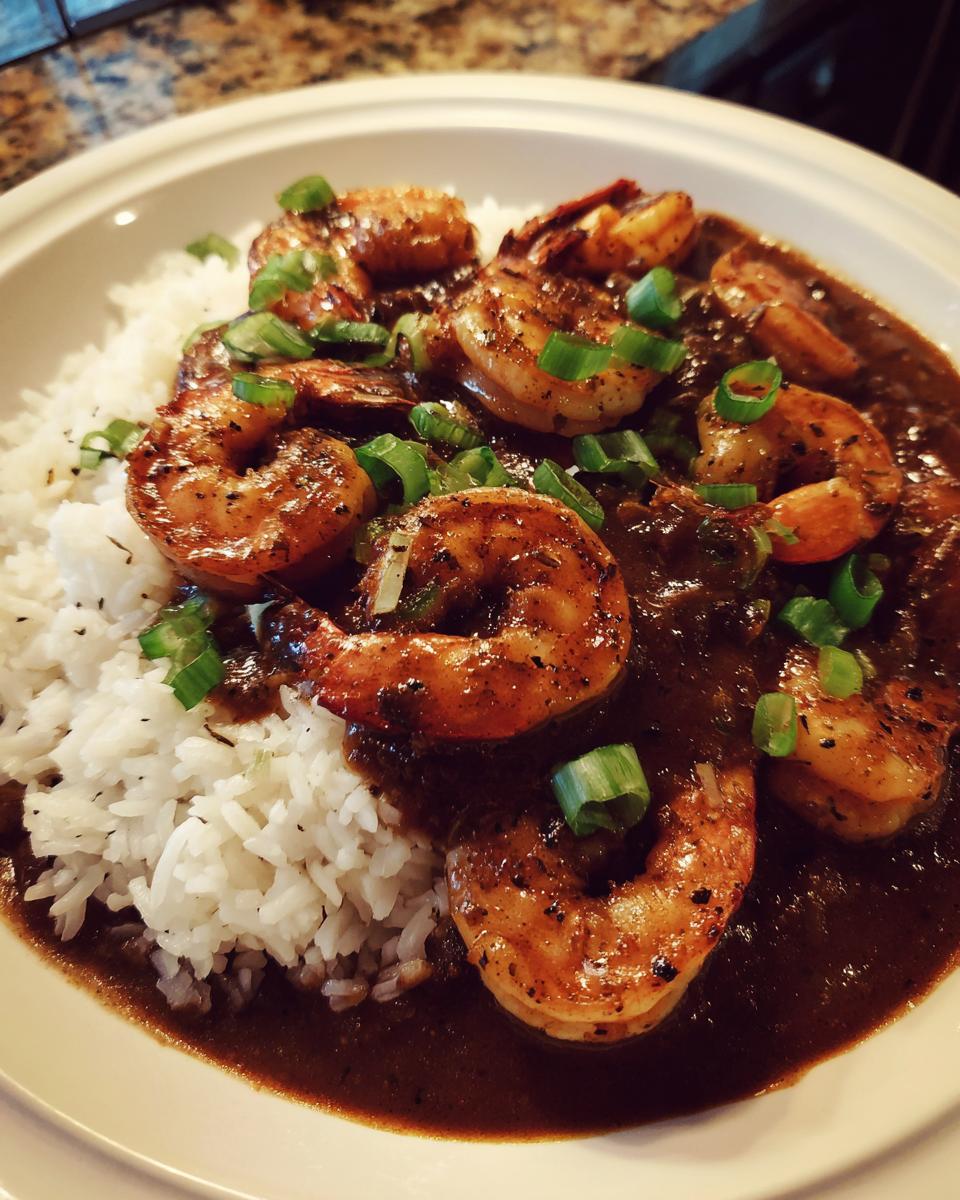 A close-up of a bowl of dark, rich shrimp etouffee served over fluffy white rice and garnished with green onions.