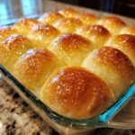 Close-up of golden brown, buttery soft rolls baked together in a glass dish, glistening with a sweet glaze.