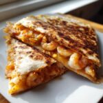Two halves of a perfectly grilled shrimp quesadilla, showing melted cheese and seasoned shrimp filling.