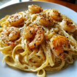 Close-up of a bowl of creamy shrimp alfredo pasta, topped with seasoned, seared shrimp.