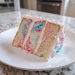 A tempting slice of multi-layered cotton candy cake showing pink and blue swirls in the white frosting and cake layers.