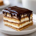 Close-up of a square slice of eclair cake showing layers of pastry, cream filling, and dripping chocolate ganache.