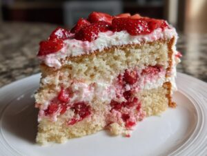Close-up of a moist slice of strawberry cake with layers of vanilla sponge, cream, and fresh strawberries.