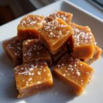A pile of soft, buttery caramels sprinkled with coarse sea salt, catching the sunlight.