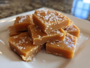 Close-up of soft, buttery caramels sprinkled with coarse sea salt, stacked on a white serving plate.
