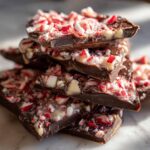 Close-up of stacked pieces of dark chocolate peppermint bark recipe topped with crushed candy canes.