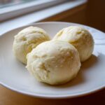 Three perfectly shaped balls of smooth, light-colored fufu dough served on a white plate.