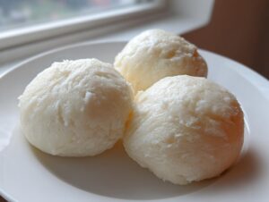 Three smooth, white scoops of freshly made fufu dough served on a white plate.
