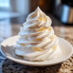 A tall, perfectly piped swirl of creamy white vanilla buttercream frosting on a small white plate.