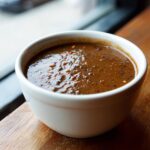 Close-up of rich, dark vegan black bean soup topped with visible pepper flakes in a white bowl.