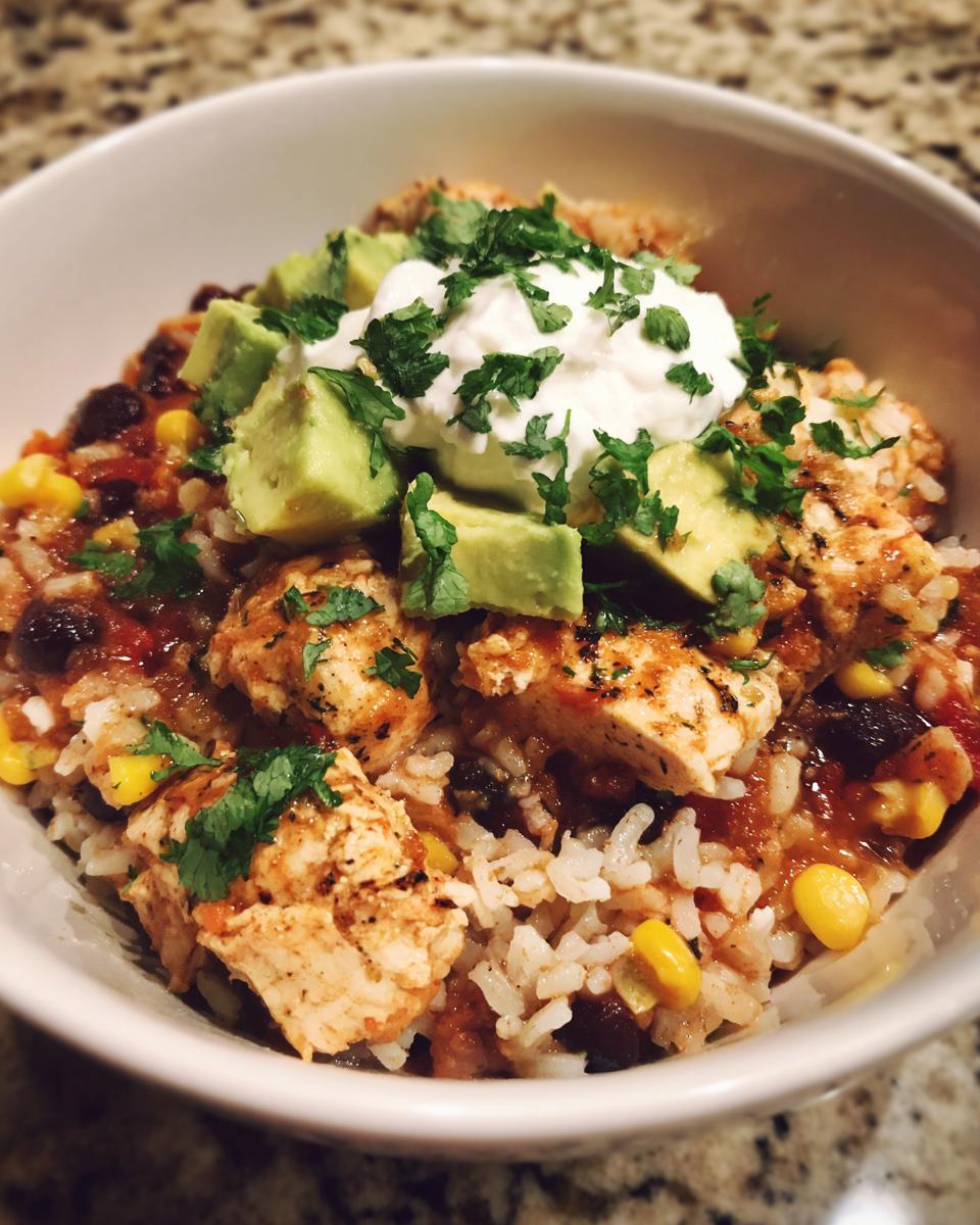 A close-up view of a delicious chicken burrito bowl featuring seasoned chicken, rice, black beans, corn, topped with avocado, sour cream, and cilantro.