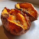 Close-up of a perfectly baked sweet potato split open, seasoned with coarse salt and pepper.