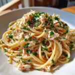 A close-up serving of creamy crab pasta, featuring spaghetti tossed in a light sauce and topped generously with flaked crab meat and fresh parsley.