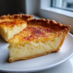 Close-up of a slice of rich buttermilk pie showing the creamy yellow filling and caramelized top crust.