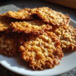 A close-up shot of several golden brown, crispy oatmeal lace cookies stacked on a white plate, catching the sunlight.