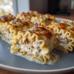Close-up of several portions of baked chicken alfredo lasagna rolls with creamy filling and browned cheese topping.