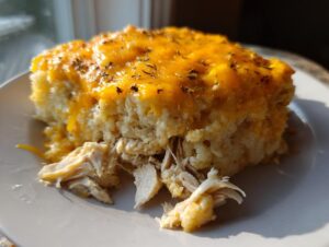 A close-up serving of chicken cauliflower rice casserole topped with melted cheddar cheese and herbs.