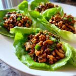 Four servings of savory chicken lettuce wraps filled with ground chicken and mushrooms, garnished with green onions.