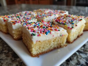 Close-up of several squares of christmas sugar cookie bars topped with white frosting and colorful sprinkles.