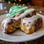 Three soft christmas tree cinnamon rolls drizzled with white icing and green sprinkles on a white plate.