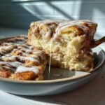 A serving of delicious cinnamon roll french toast being lifted, showing a thick, gooey icing drip.