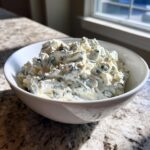 A close-up of chunky, creamy blue cheese dip loaded with visible blue cheese crumbles in a white bowl.