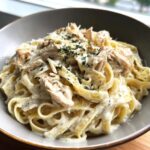 A close-up of creamy chicken fettuccine alfredo topped with shredded chicken and fresh parsley.