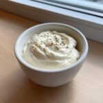 A small white bowl filled with thick, white creamy horseradish sauce, garnished with dried herbs and pepper flakes.