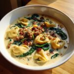 Close-up of a bowl of creamy italian sausage tortellini soup with spinach and sun-dried tomatoes.