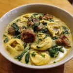 Close-up of a hearty bowl of creamy sausage tortellini soup featuring browned sausage chunks and wilted spinach.