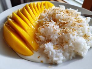 Close-up of vibrant mango sticky rice, featuring sliced fresh mango next to coconut rice topped with toasted sesame seeds.