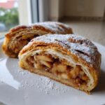 Close-up of two slices of flaky apple strudel dusted generously with powdered sugar.