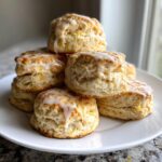 A stack of fluffy, golden scones topped with a sweet white lemon glaze on a white plate.