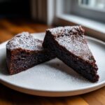 Two rich, dark slices of flourless chocolate cake dusted with powdered sugar on a white plate.