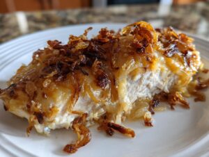 A close-up, cross-section view of a tender piece of french onion chicken topped with melted cheese and crispy fried onions.