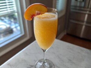 A frozen, slushy peach bellini recipe served in a champagne flute, garnished with a fresh peach slice.