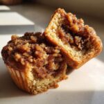 Close-up of a pecan pie muffin cut in half, showing the gooey brown sugar filling and crumb topping.