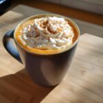 A close-up of a homemade pumpkin spice latte topped with whipped cream and cinnamon spice.